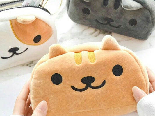 3 cat plush pencil cases. One is on the left and is white with ginger spots, the middle is being held and is ginger and the right is black. All feature cute cat faces from the Neko Atsume game