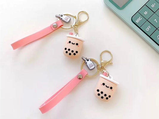 2 keychains, each has a smiley faced bubble milk tea charm, a pink fob and a mini milk charm all on a gold coloured keychain