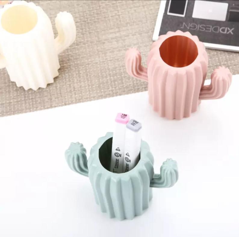 aerial view of 3 cactus shaped pen pots in 3 different colours, blue-grey, pink and white. The blue-grey pen pot has 2 copic markers inside and the others are empty.