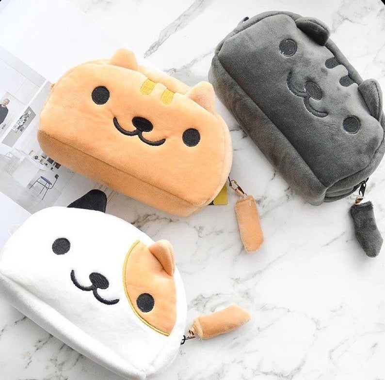3 cat plush pencil cases lying on a marble background. The bottom is a calico cat, the middle is ginger and the top is black