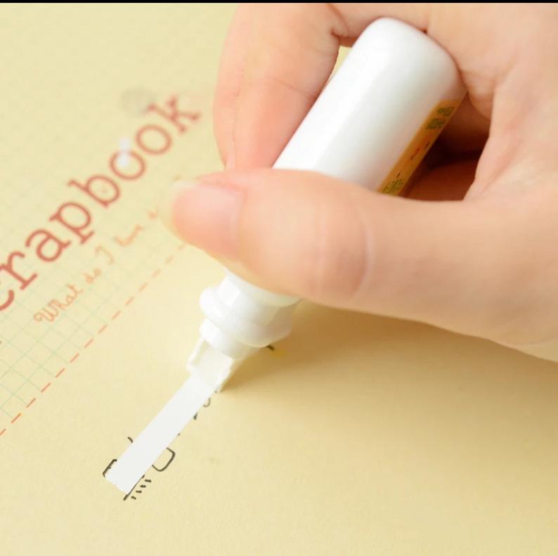 a banana milk correction tape being used to remove a writing peen mistake on a yellow scrapbook